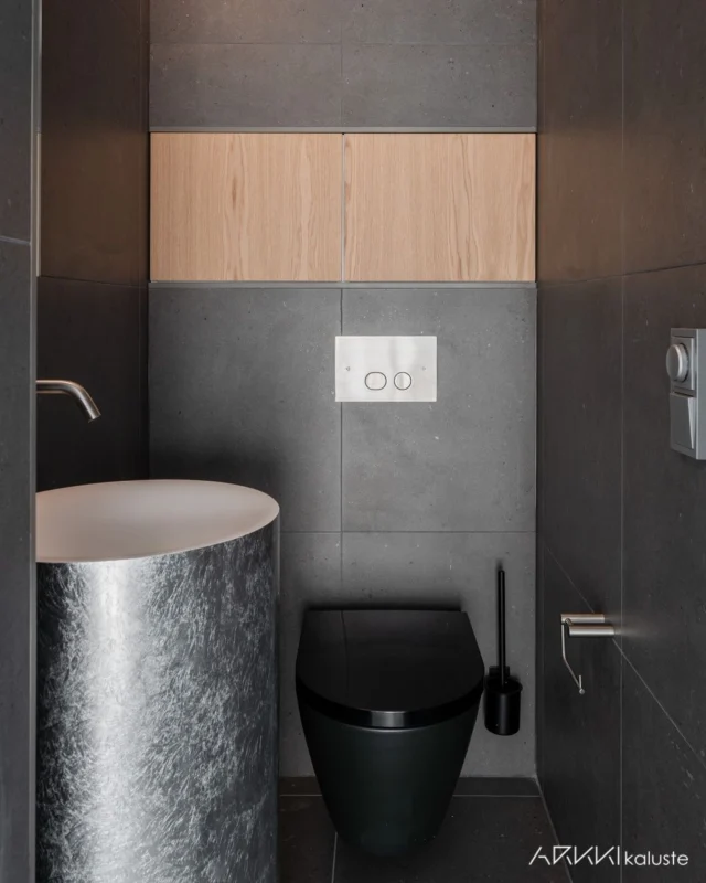 Tämä kompakti WC hurmaa materiaalivalinnoilla ja viimeistellyillä yksityiskohdilla. WC-koteloinnin yläpuolelle toteuttamamme kaappi tuo tilaan minimalistista ja huomaamattomasti integroitua säilytystilaa. Tammiset ovet tuovat tummasävyiseen kokonaisuuteen lämpimän ja luonnollisen vivahteen. 🩶 Suunnittelu: @studioilkkapalinpera Kuvaus: @virtualstudio.fi #arkkikaluste #mittatilauskaluste #mittatilauskalusteet #kylpyhuonekalusteet #kylpyhuoneratkaisut #suomalaistakäsityötä #madeinfinland #designfromfinland‌